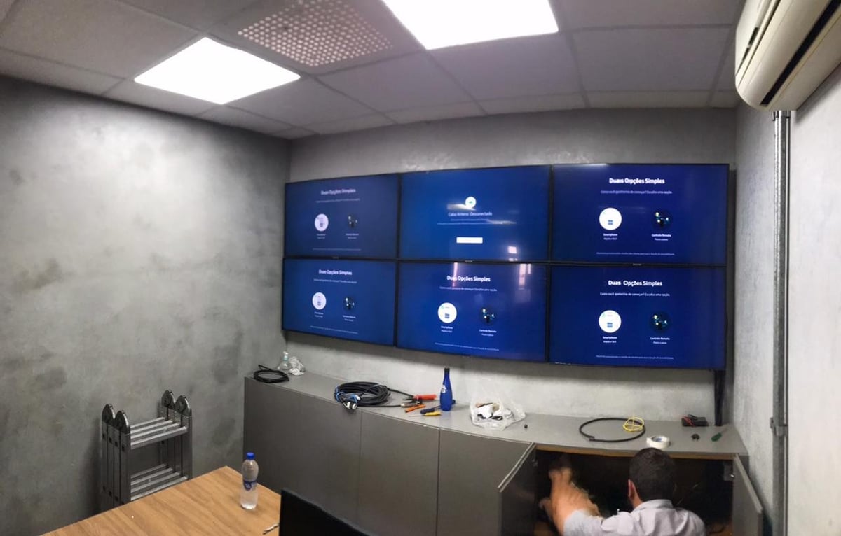 Modern office room with six blue display monitors mounted on concrete wall above counter with equipment and desk