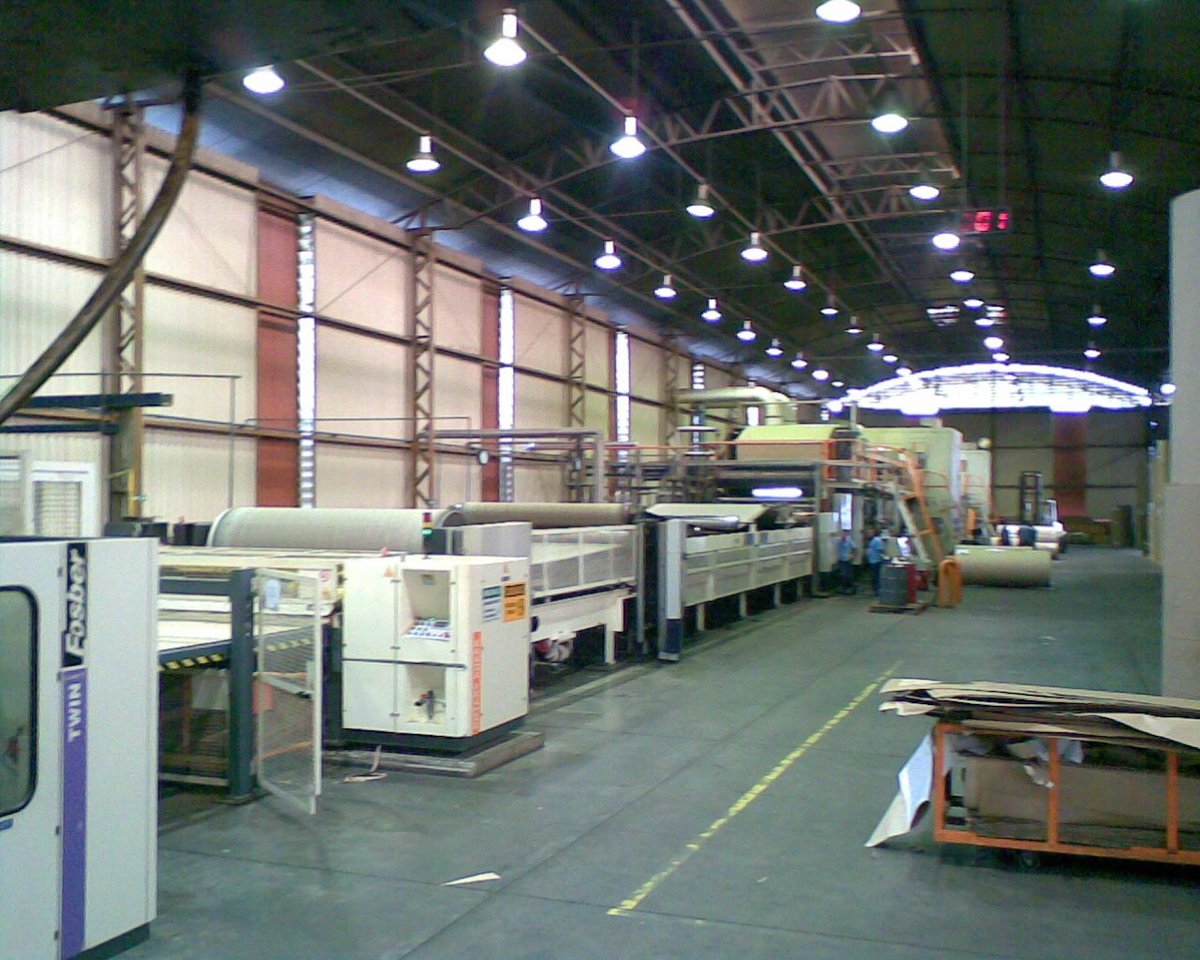 Industrial manufacturing facility with large CNC machines and equipment lined up on factory floor under bright overhead lighting