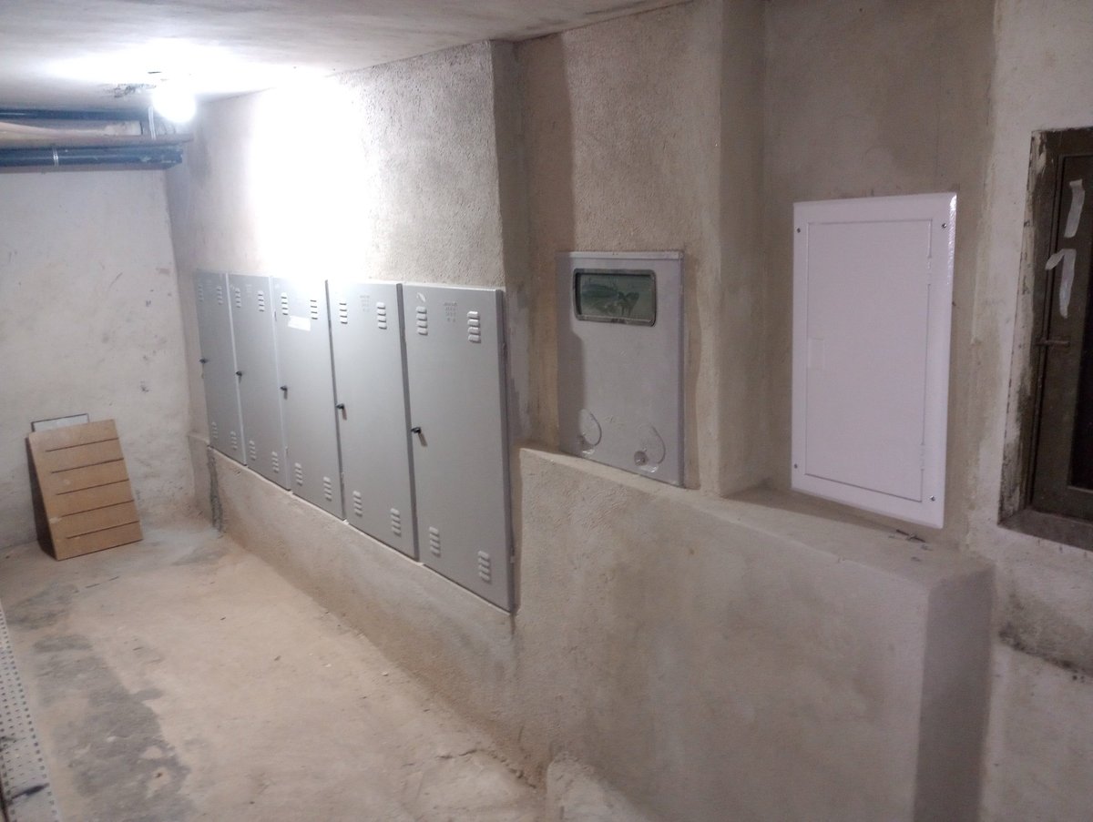 Unfinished concrete basement room with metal lockers and thermostat on wall