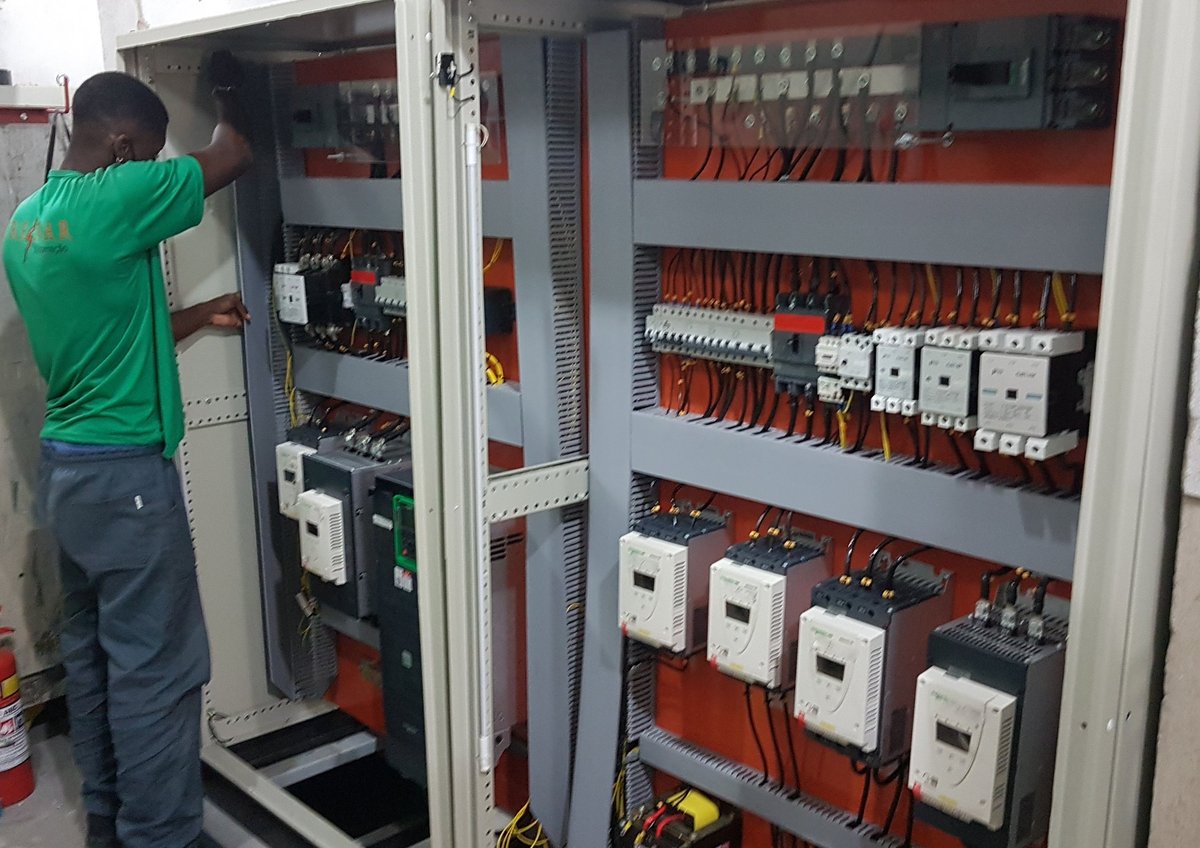 Technician in green shirt working on an industrial electrical control panel with circuit breakers and switches